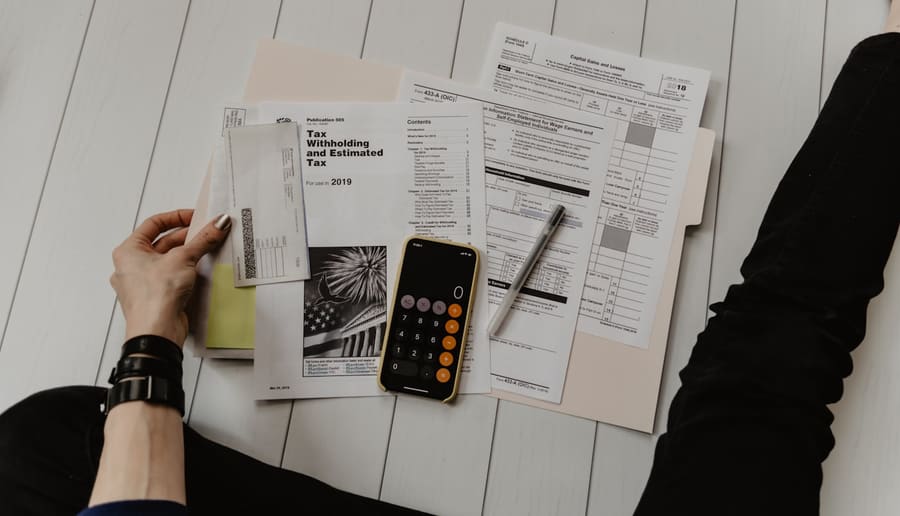 Vista de cima de formulários financeiros impressos, calculadora e caneta sobre uma mesa de trabalho