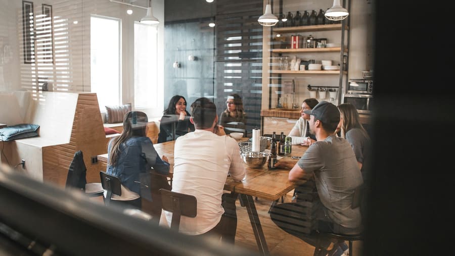 Equipe reunida em torno de uma mesa longa de trabalho, vista através de uma parede de vidro