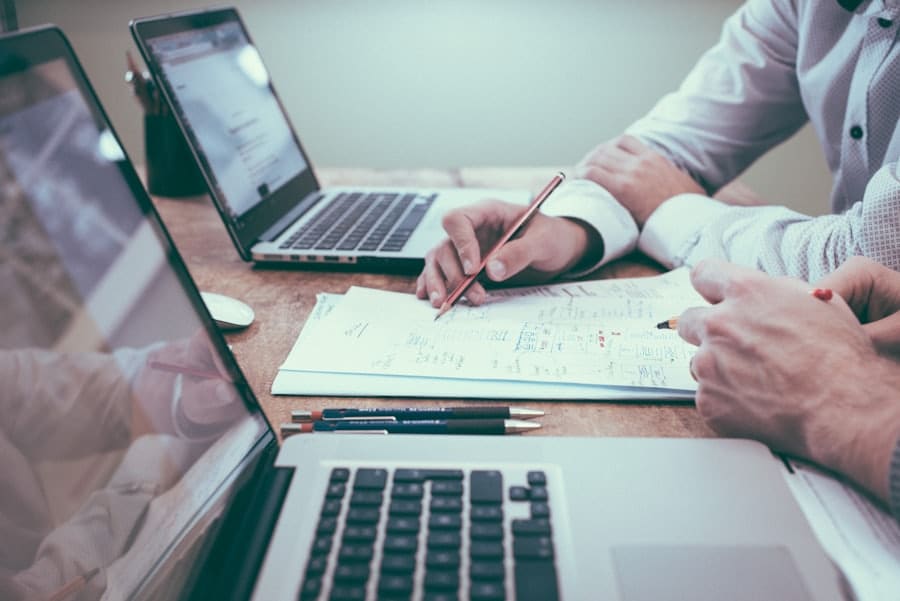 Mesa de trabalho com planilhas impressas, notebooks e canetas durante uma análise
